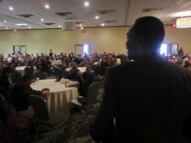 A speaker addressing a large audience in a conference room.