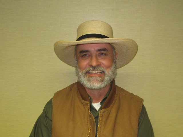 A smiling man wearing a wide-brimmed hat and brown vest.