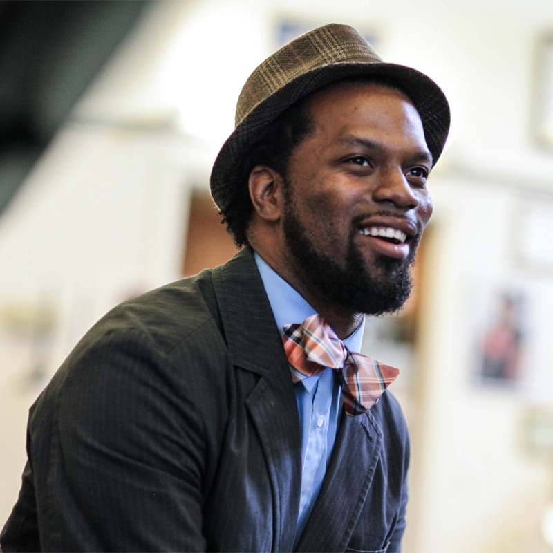 A smiling man wearing a hat and bow tie.
