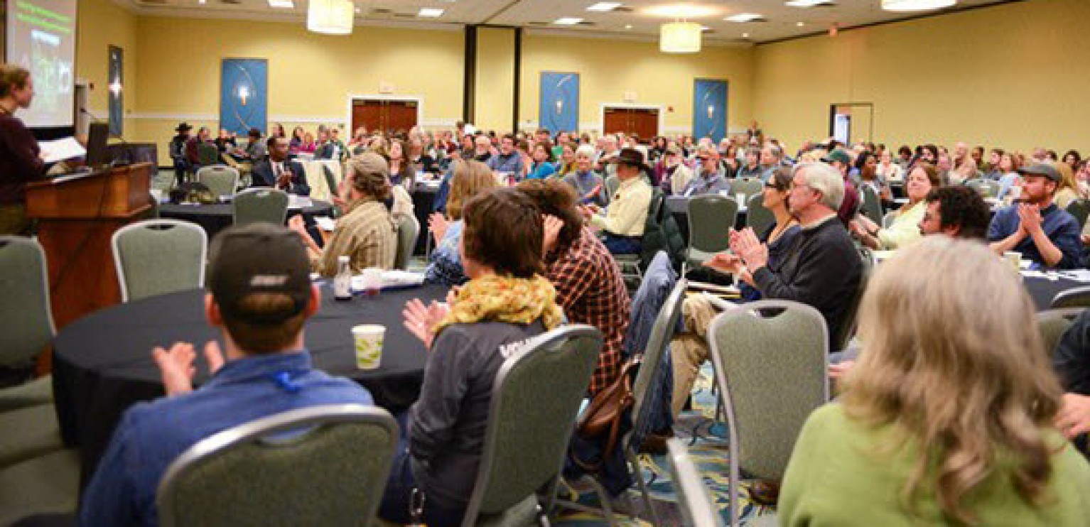 A large group of people seated at round tables in a conference room.