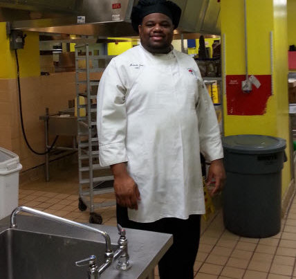 Chef in white uniform standing in a commercial kitchen.