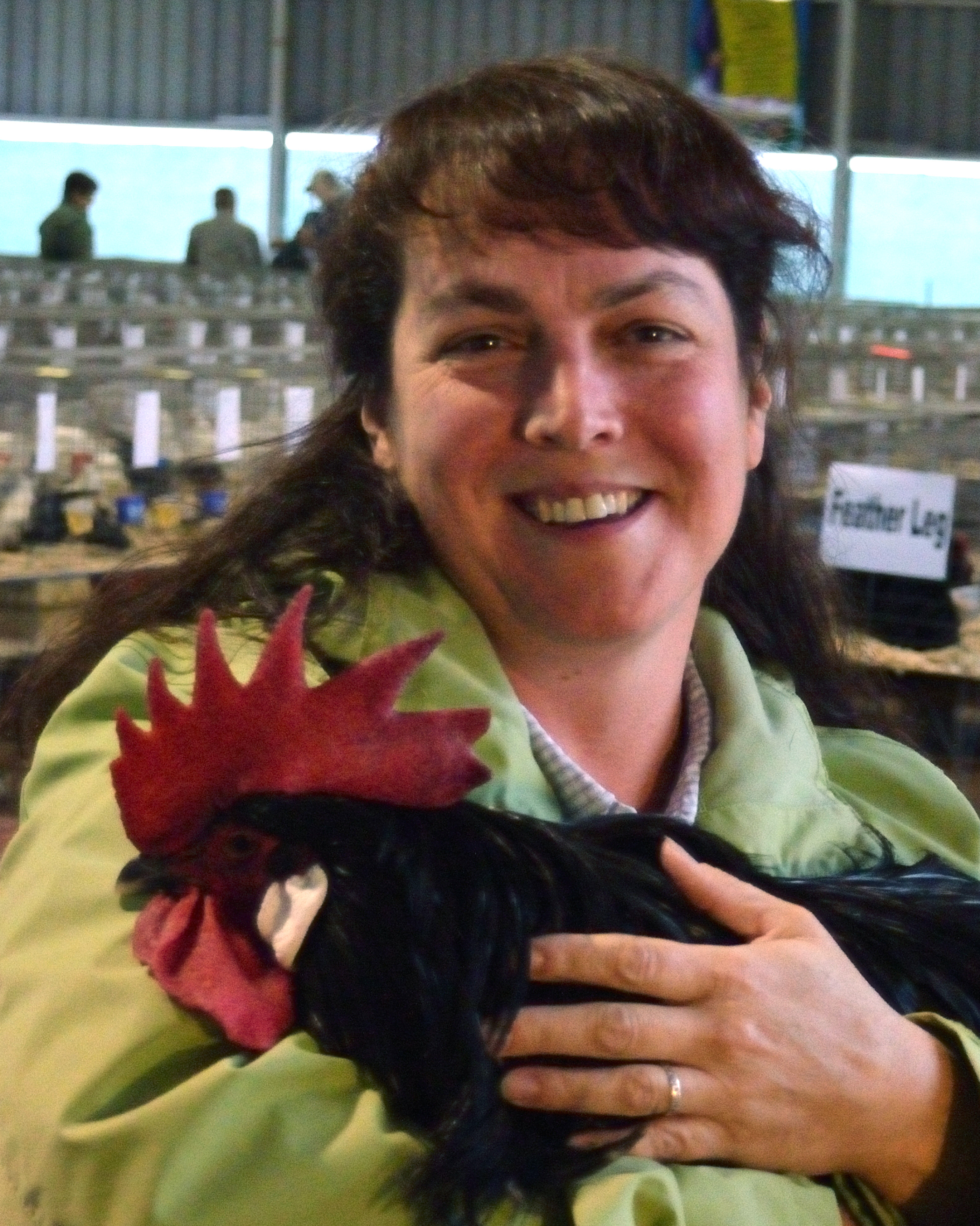 A woman smiling while holding a black rooster with a red comb.