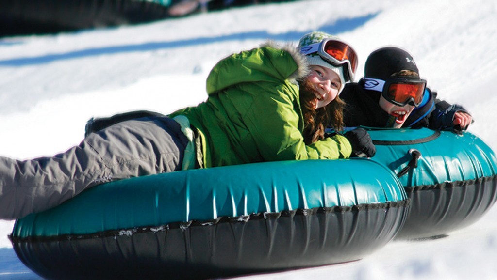 Two people enjoying snow tubing on a sunny winter day.