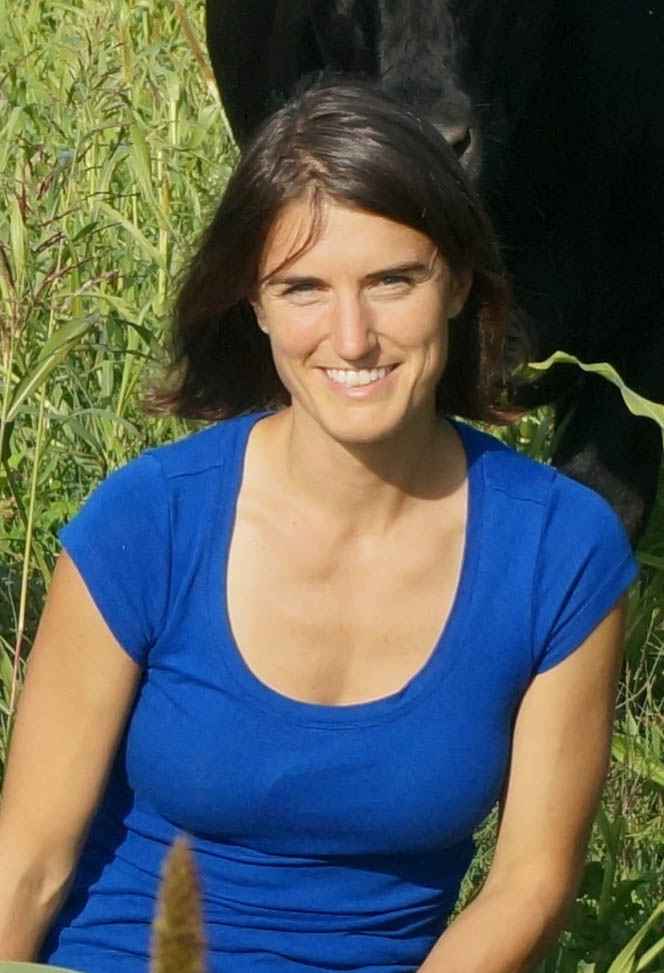 A woman with brown hair wearing a blue shirt outdoors.