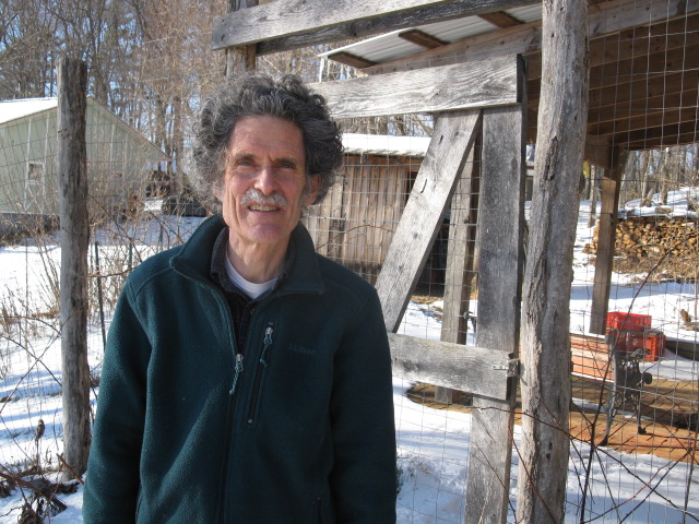 A man standing outdoors near a wooden structure in a snowy area.