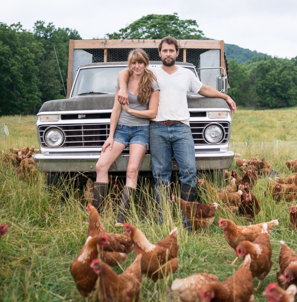A couple standing by a truck surrounded by chickens.