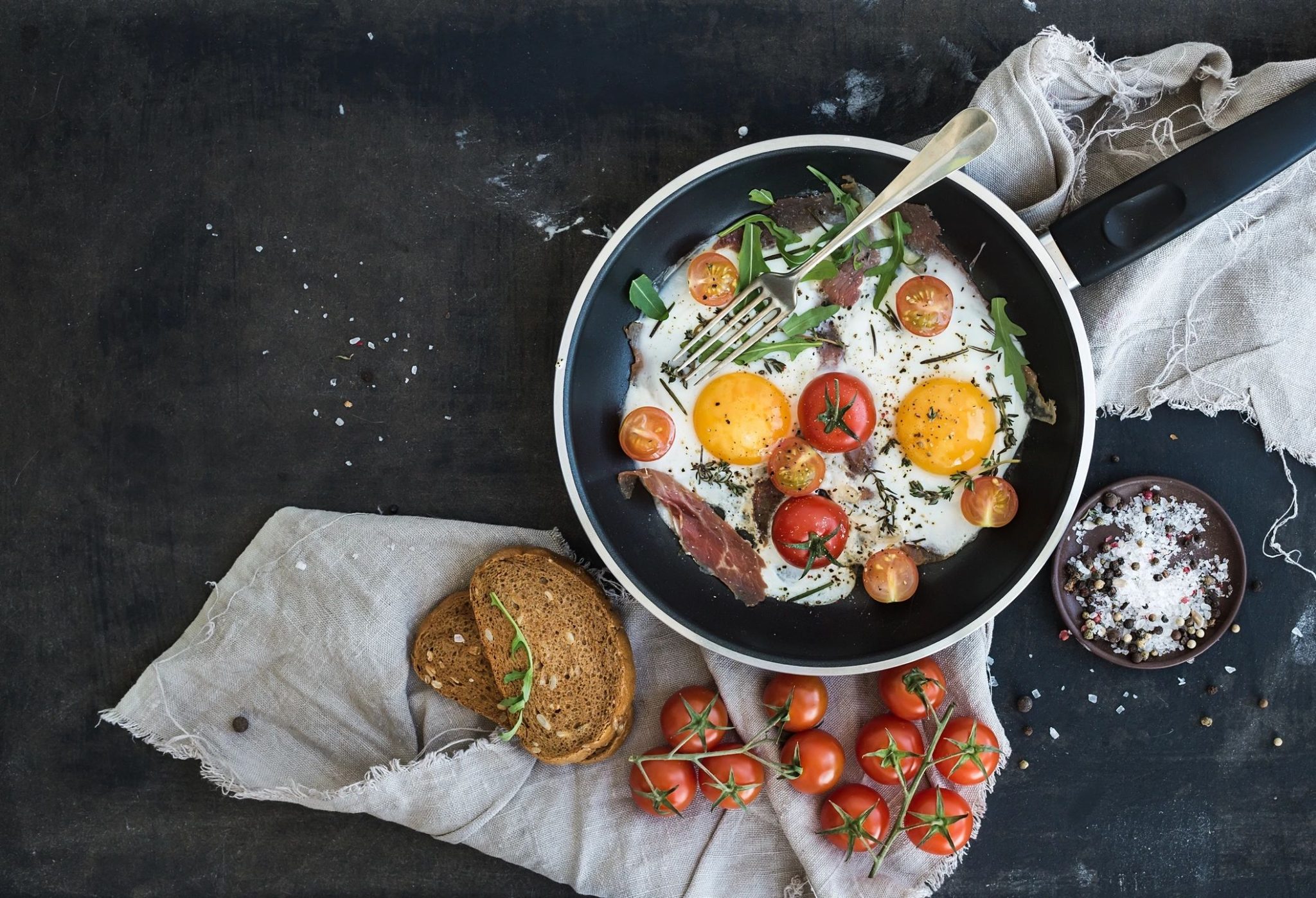 A bowl of tomato soup with croutons and herbs beside cherry tomatoes and bread.