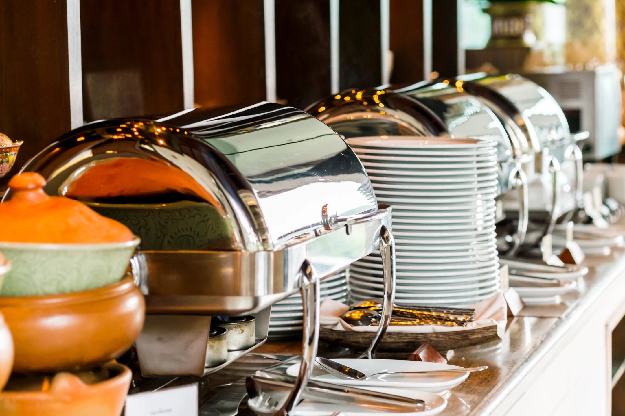 Buffet setup with chafing dishes and stacked white plates.