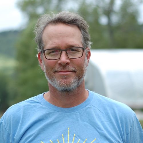 A middle-aged man wearing glasses and a blue shirt outdoors.