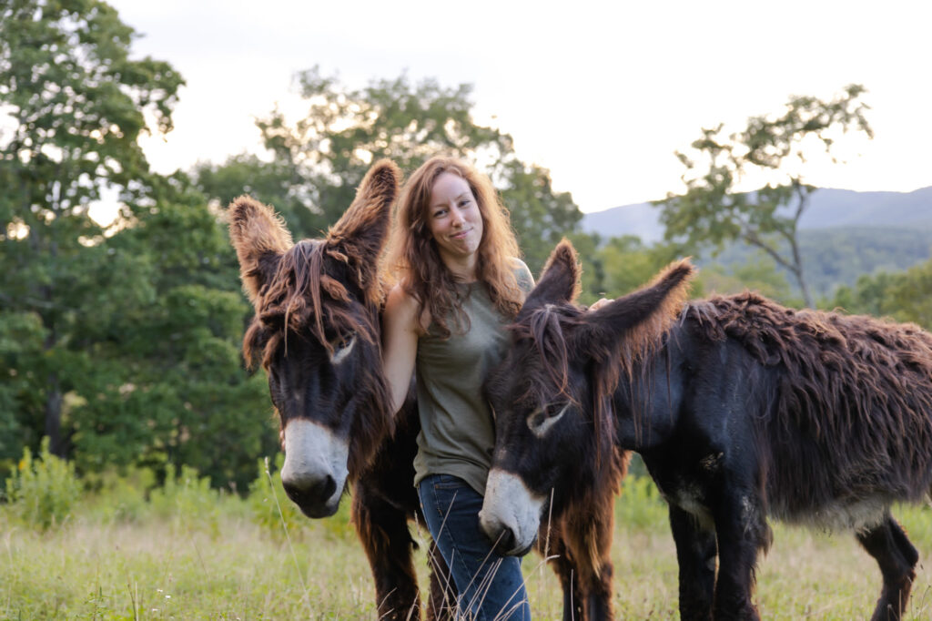 A woman standing outdoors with two donkeys.
