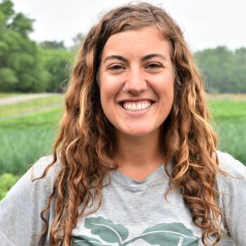 A smiling woman with long curly hair standing outdoors.
