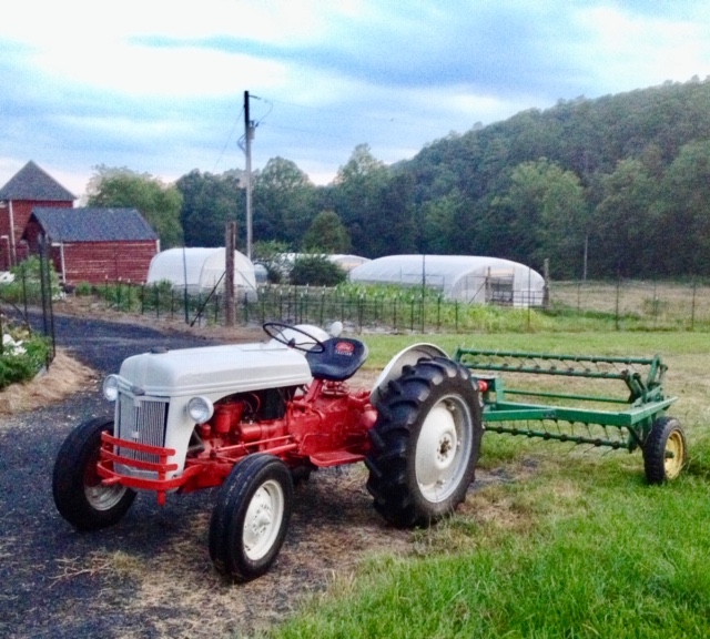 A red and white tractor parked on a grassy field with farming equipment attached.