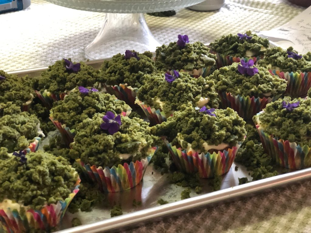 Green cupcakes with purple flower decorations on a tray.