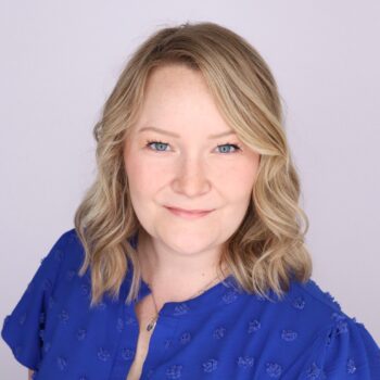 A woman with blonde hair wearing a blue top smiles at the camera.