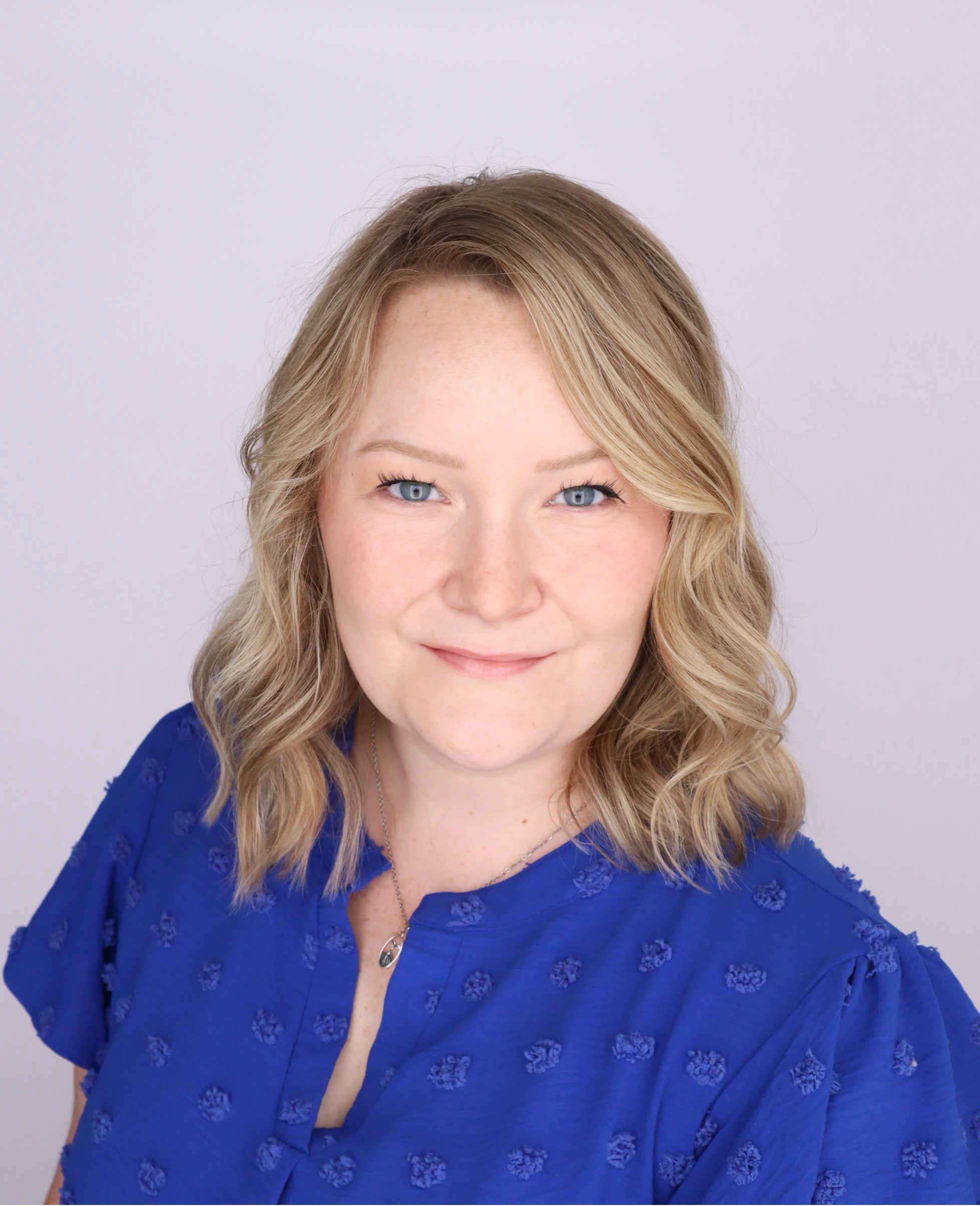 A woman with blonde hair wearing a blue top smiles at the camera.