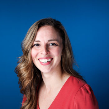 A smiling woman with wavy hair against a blue background.