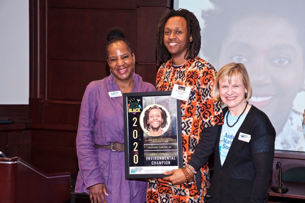 Three women smiling, holding an award plaque.