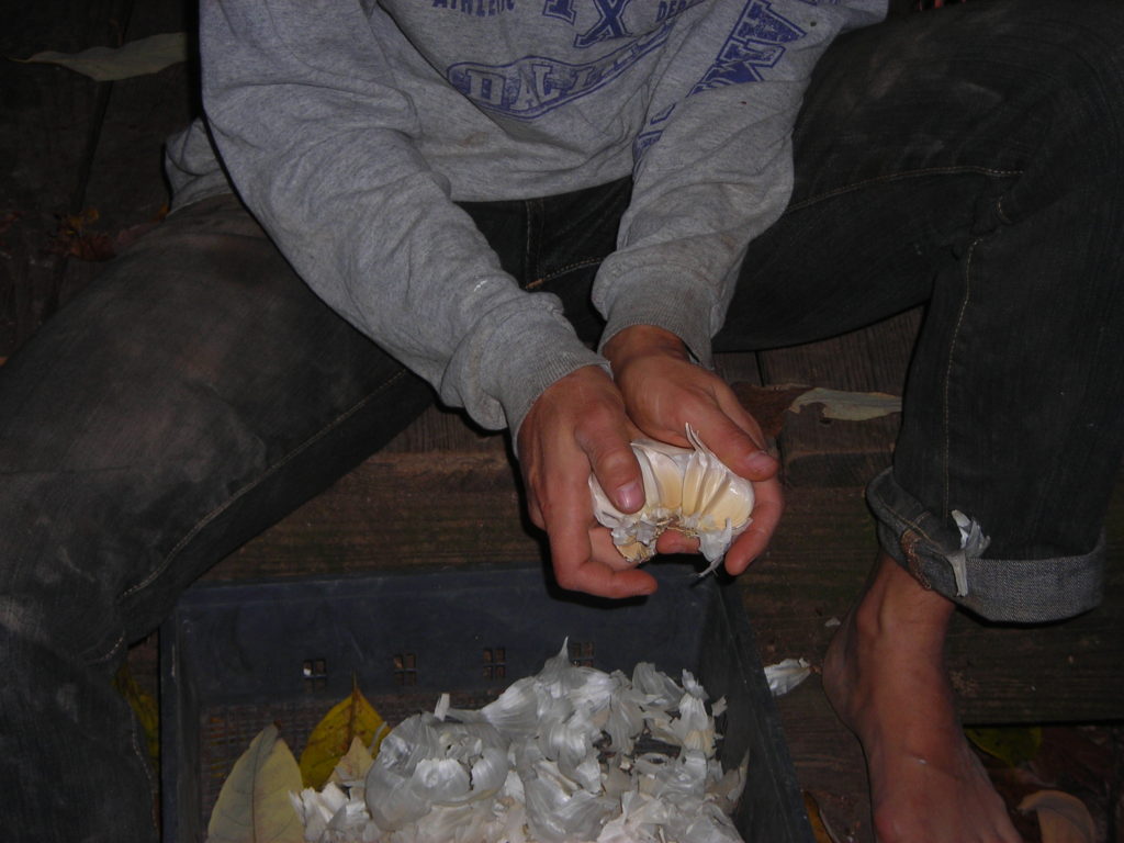 A person holding a peeled orange over a trash bin.