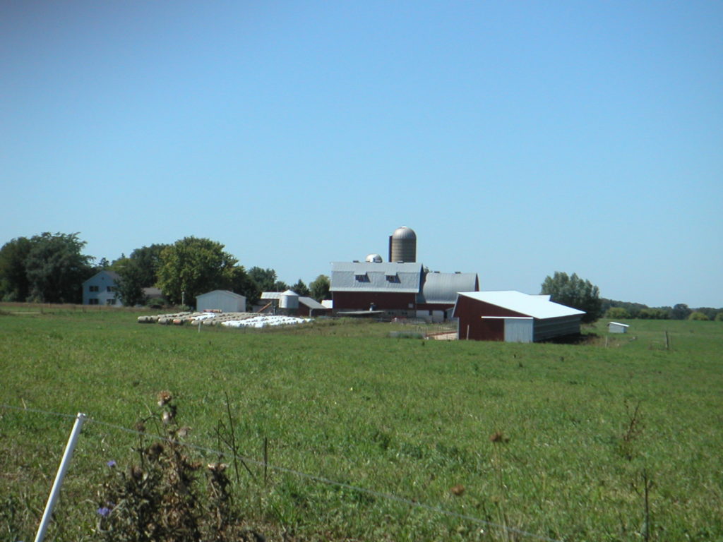 A farm with red and white buildings under a clear blue sky.
