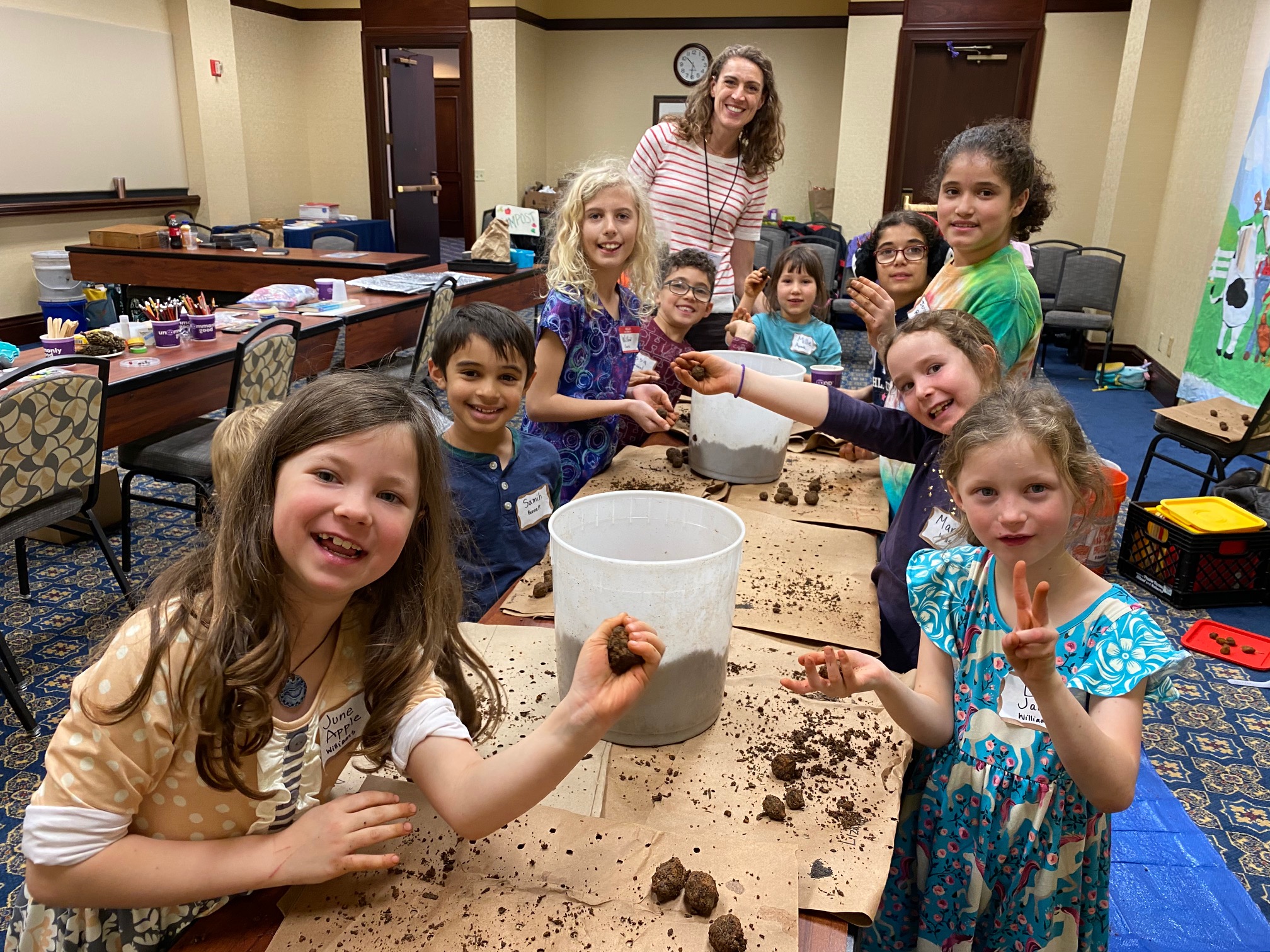 Children and an adult making clay pots together indoors.