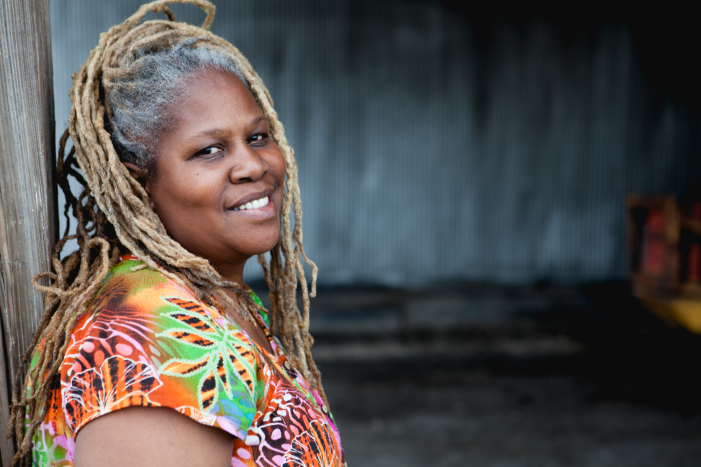 Smiling woman with long braided hair and colorful clothing.