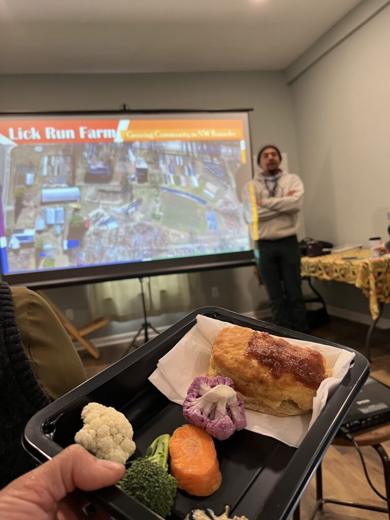 A man stands in front of a screen showing a live feed of a market, with food in the foreground.