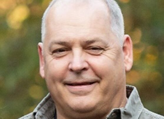 Smiling middle-aged man outdoors with blurred greenery background.