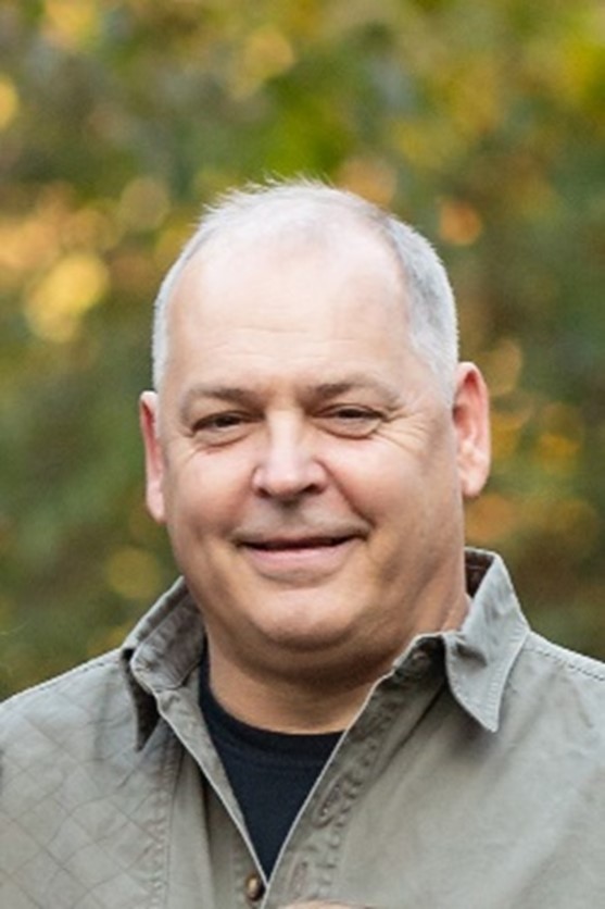 Smiling middle-aged man outdoors with blurred greenery background.